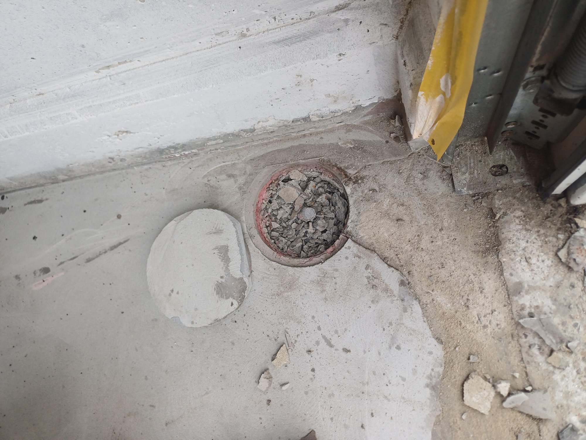 Rundes Bodenloch mit Bauschutt in Betonboden neben Metallprofil und gelber Folie