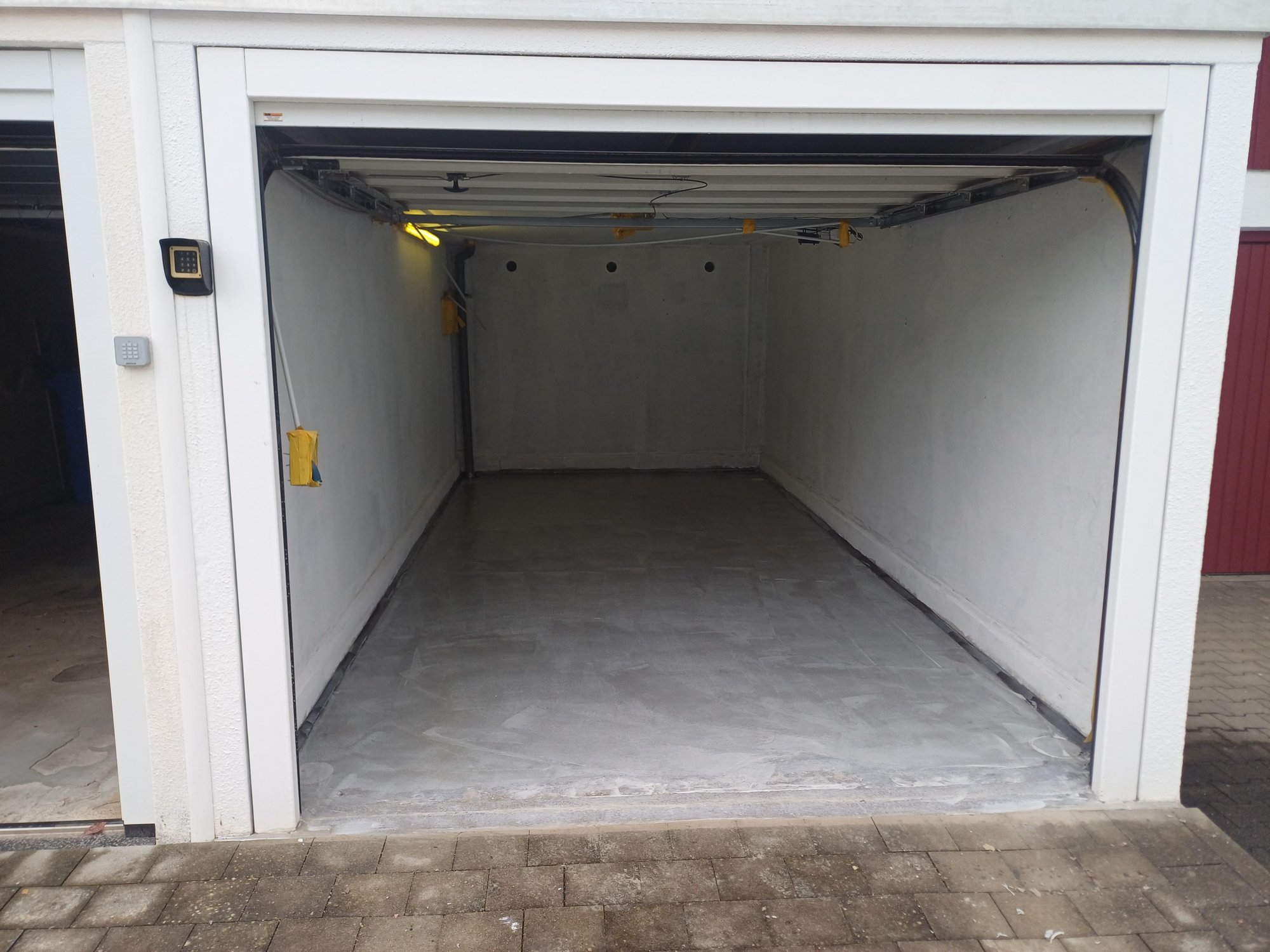 Leere Garage mit grauem Boden und weißen Wänden, Garagentor geöffnet