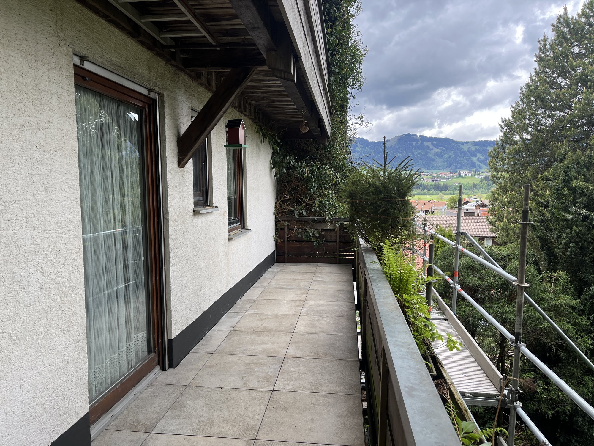 Balkon mit Fliesenboden am Haus, Geruest am Gelaender, Blick auf Berge