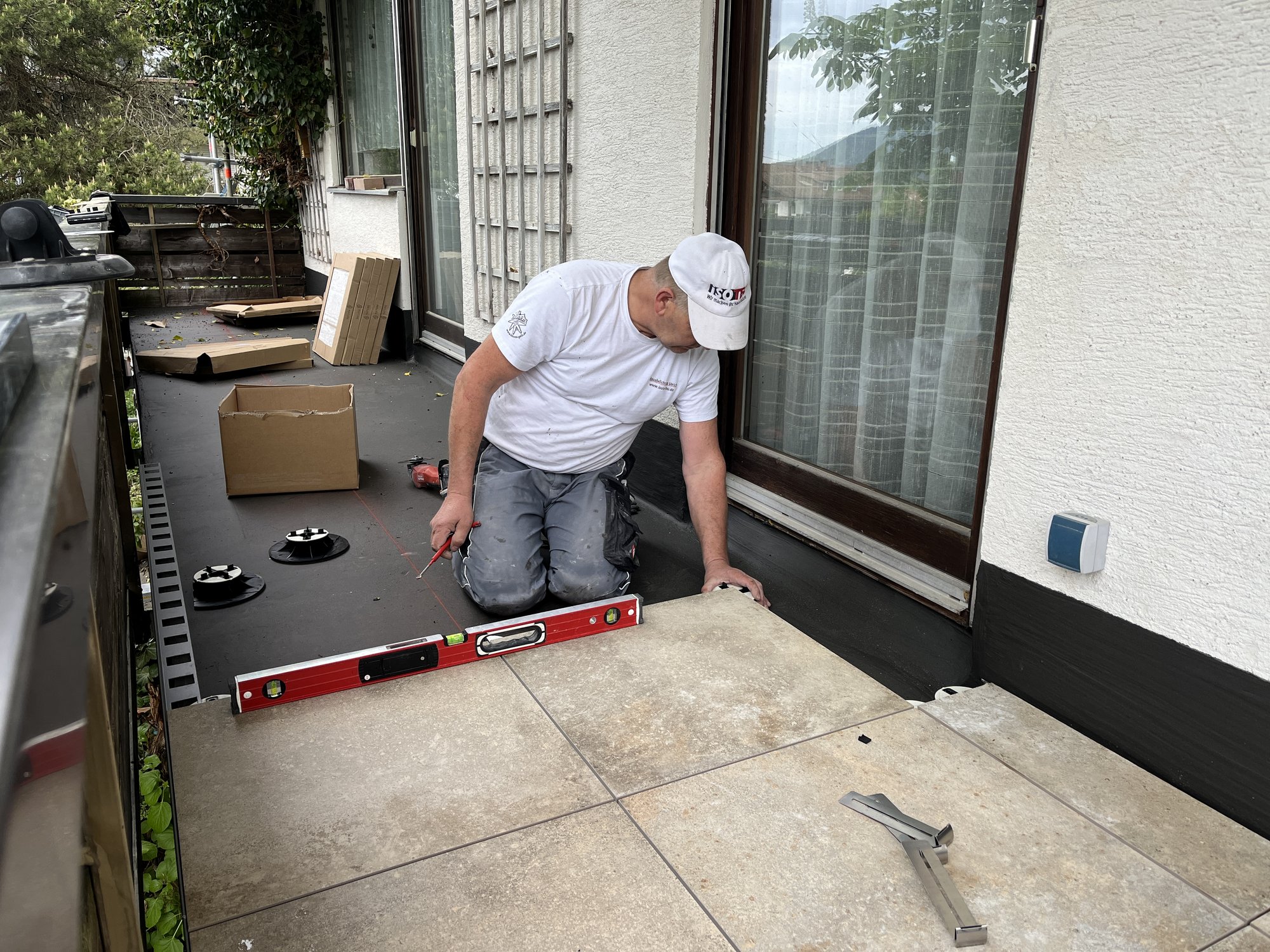 ISOTEC Mitarbeiter richtet Terrassenplatten mit Wasserwaage am Fenster aus.