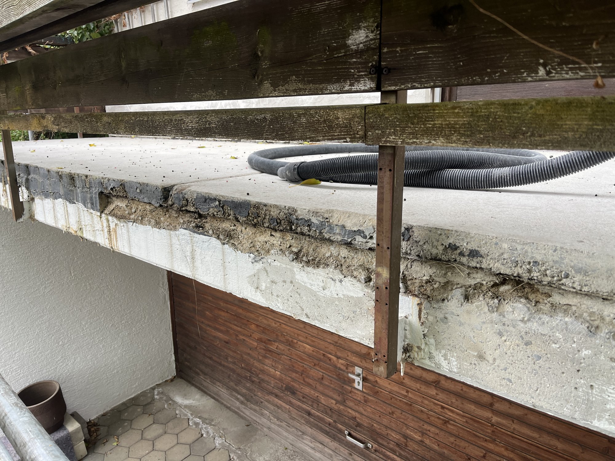 Beschädigte Betonkante am Balkon, schwarze Schlauchleitung auf Betonplatte.