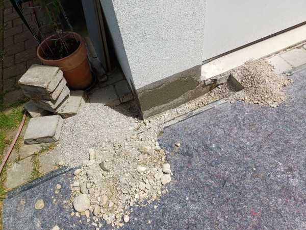 Freigelegter Sockelbereich am Gebäude, Kies und Betonplatten am Boden