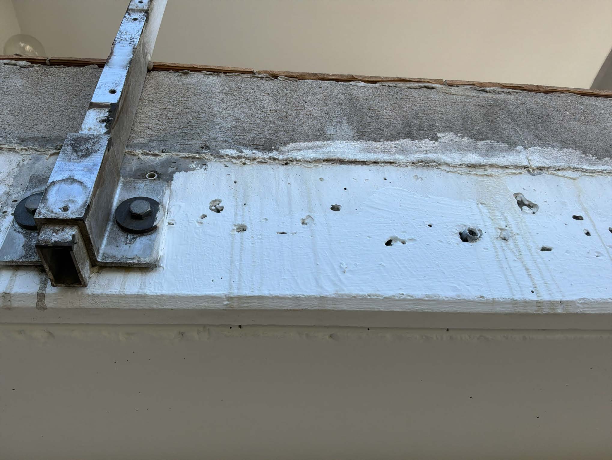 Stahlträger mit Schrauben auf weiß beschichteter Betonfläche, Bohrlöcher sichtbar