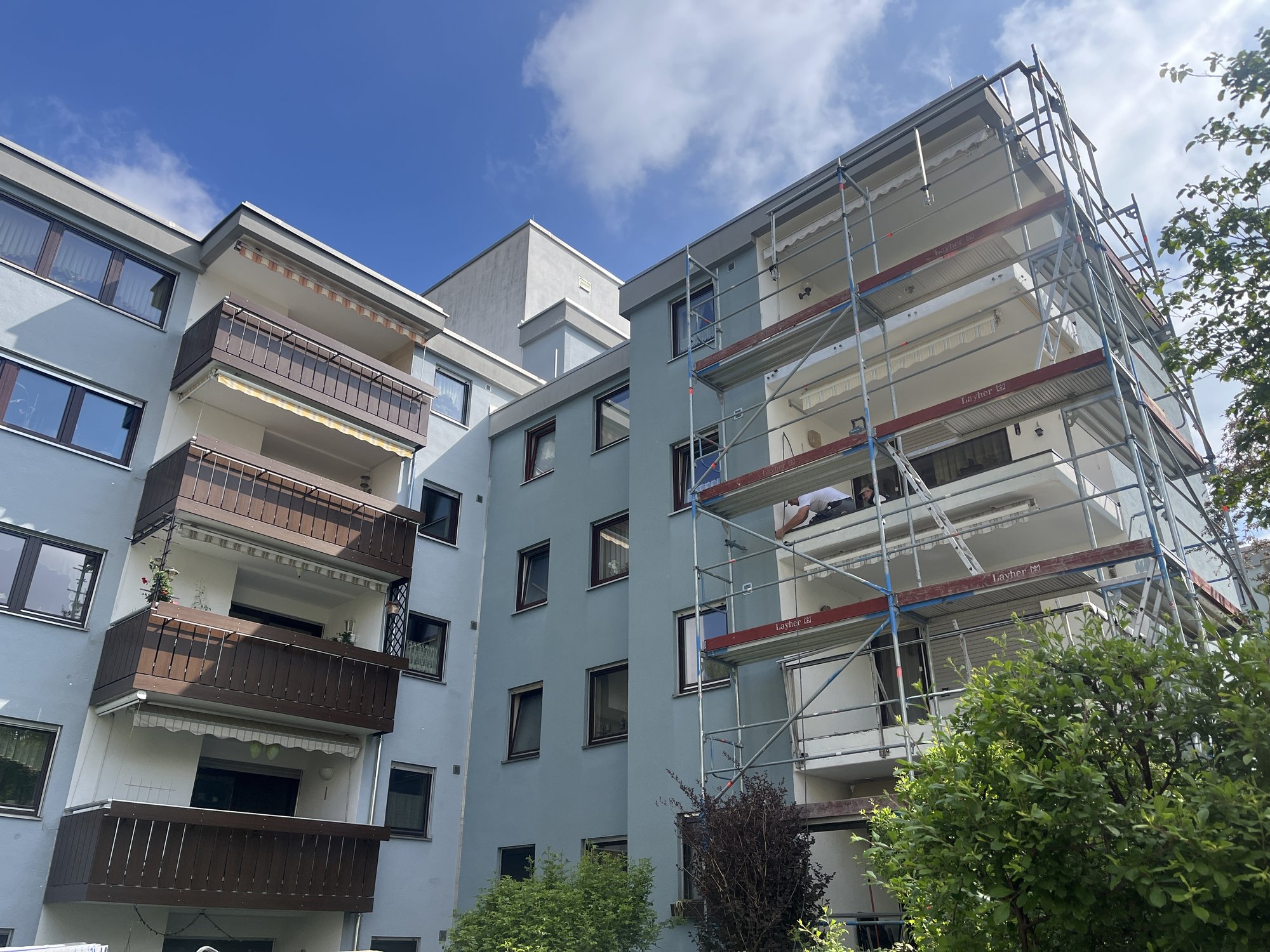 Mehrfamilienhaus mit Baugeruest an Balkonen, Arbeiter arbeitet am Balkonunterbau.