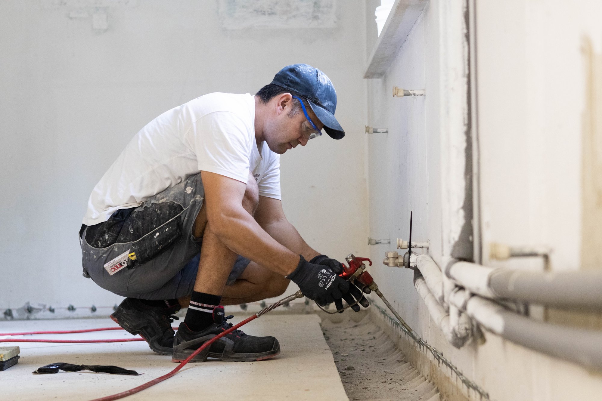Handwerker schneidet Rohrleitung mit Rohrschneider an Kellerwand, Schutzbrille und Handschuhe
