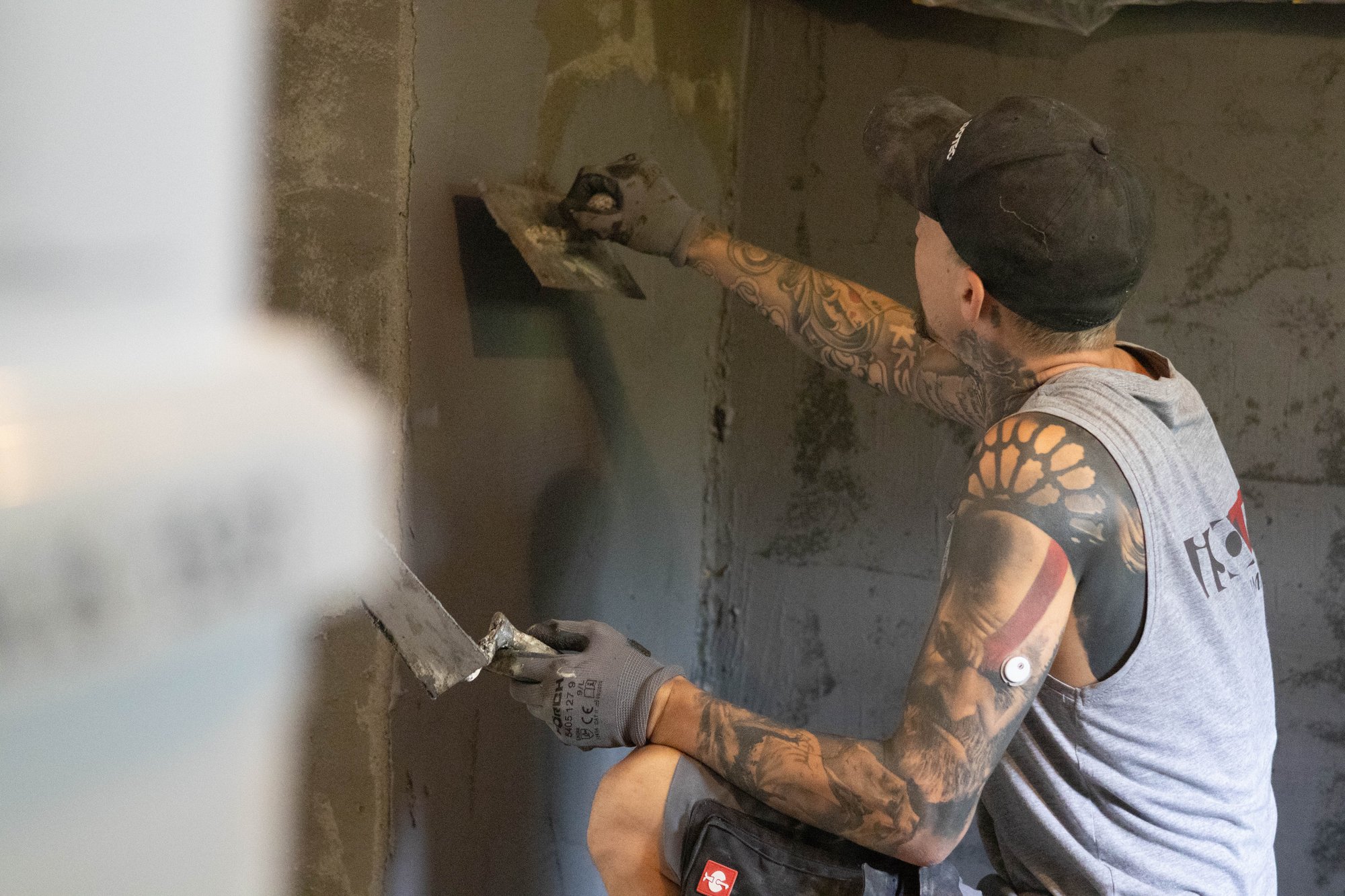 Arbeiter trägt graue Masse mit Glättkelle auf Wand auf.