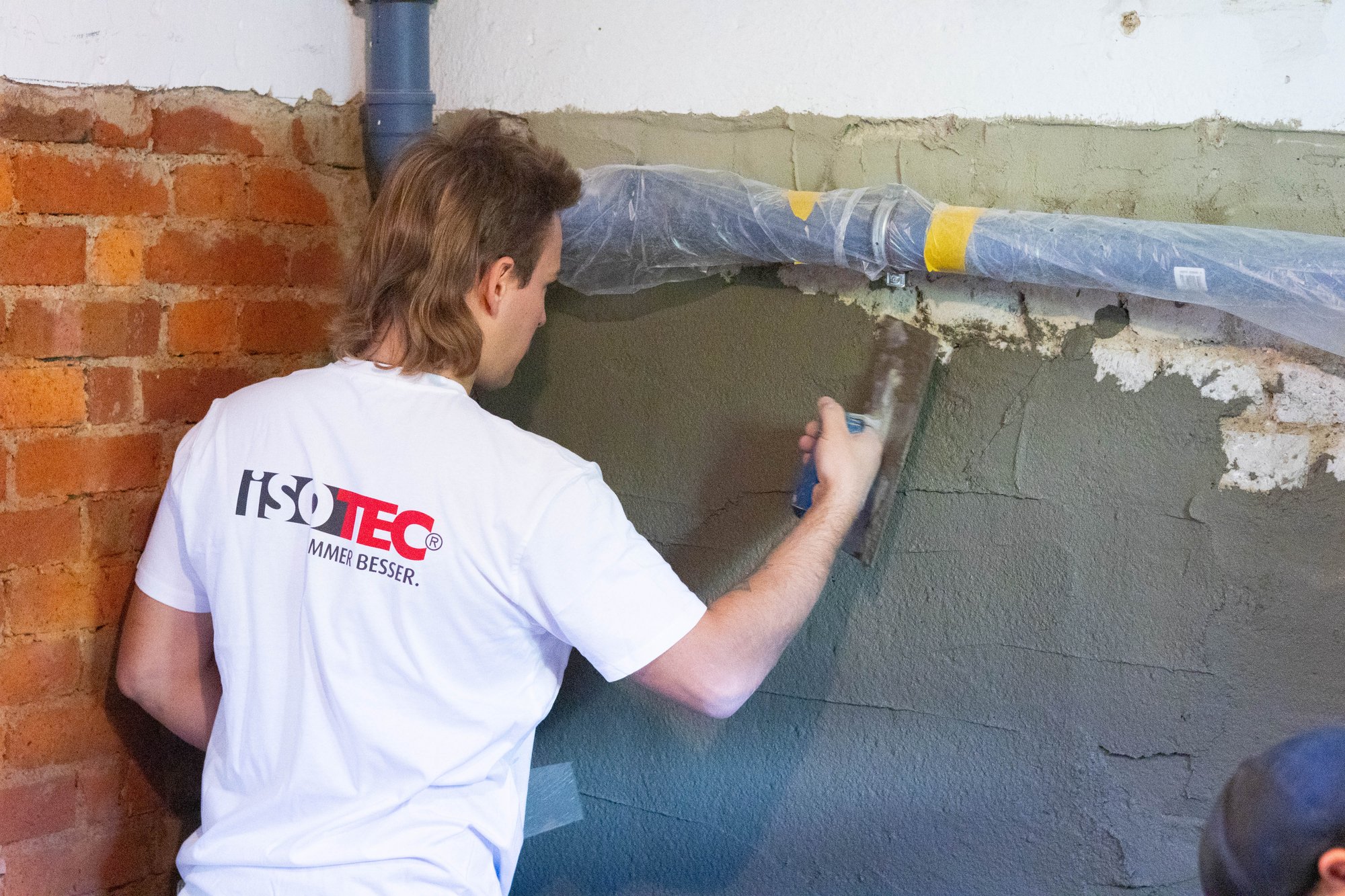 ISOTEC Mitarbeiter trägt graue Masse auf Kellerwand auf.