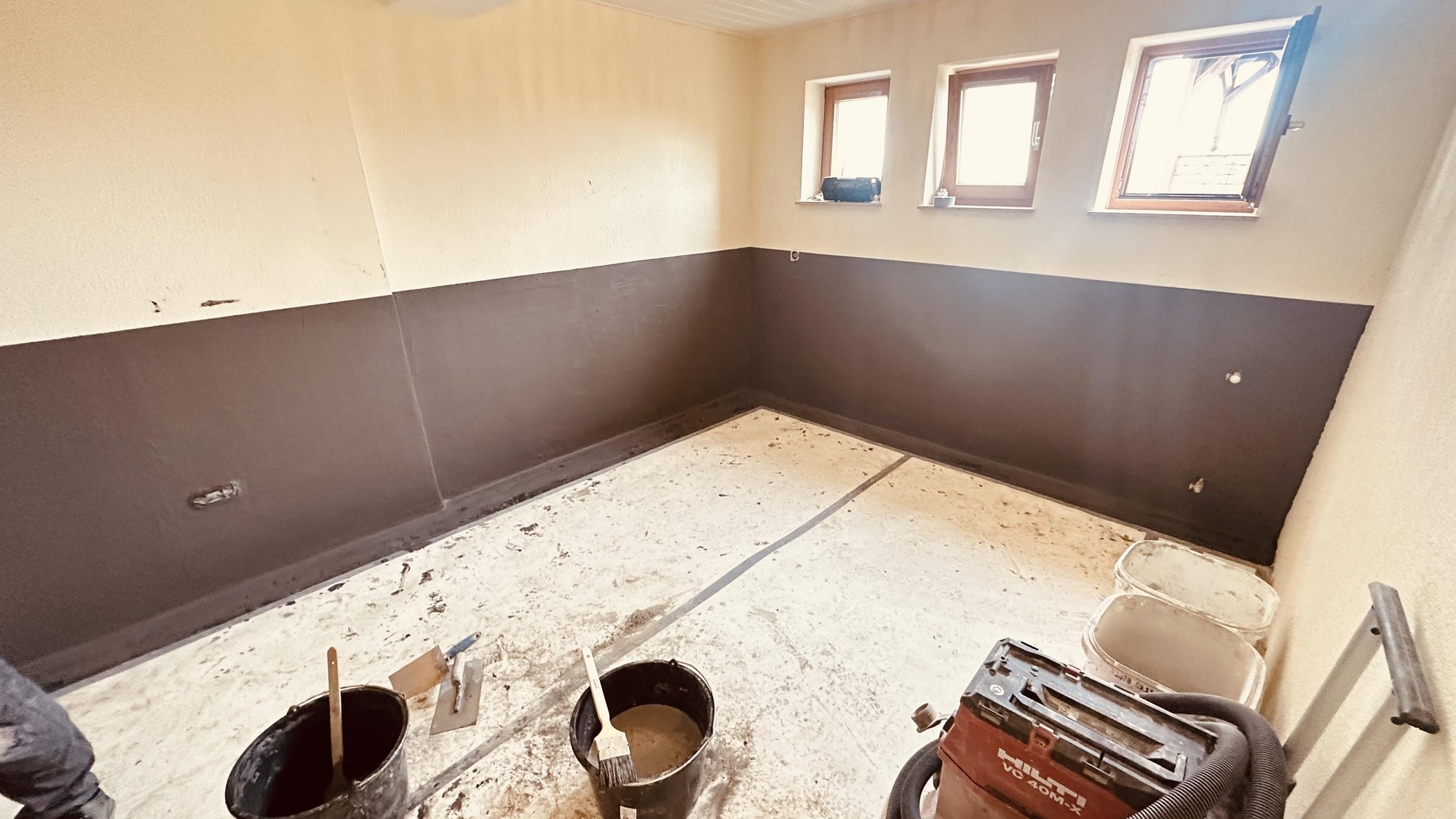 Zimmer mit brauner Wandbeschichtung, Eimer, Kellen und Baustellengerat am Boden