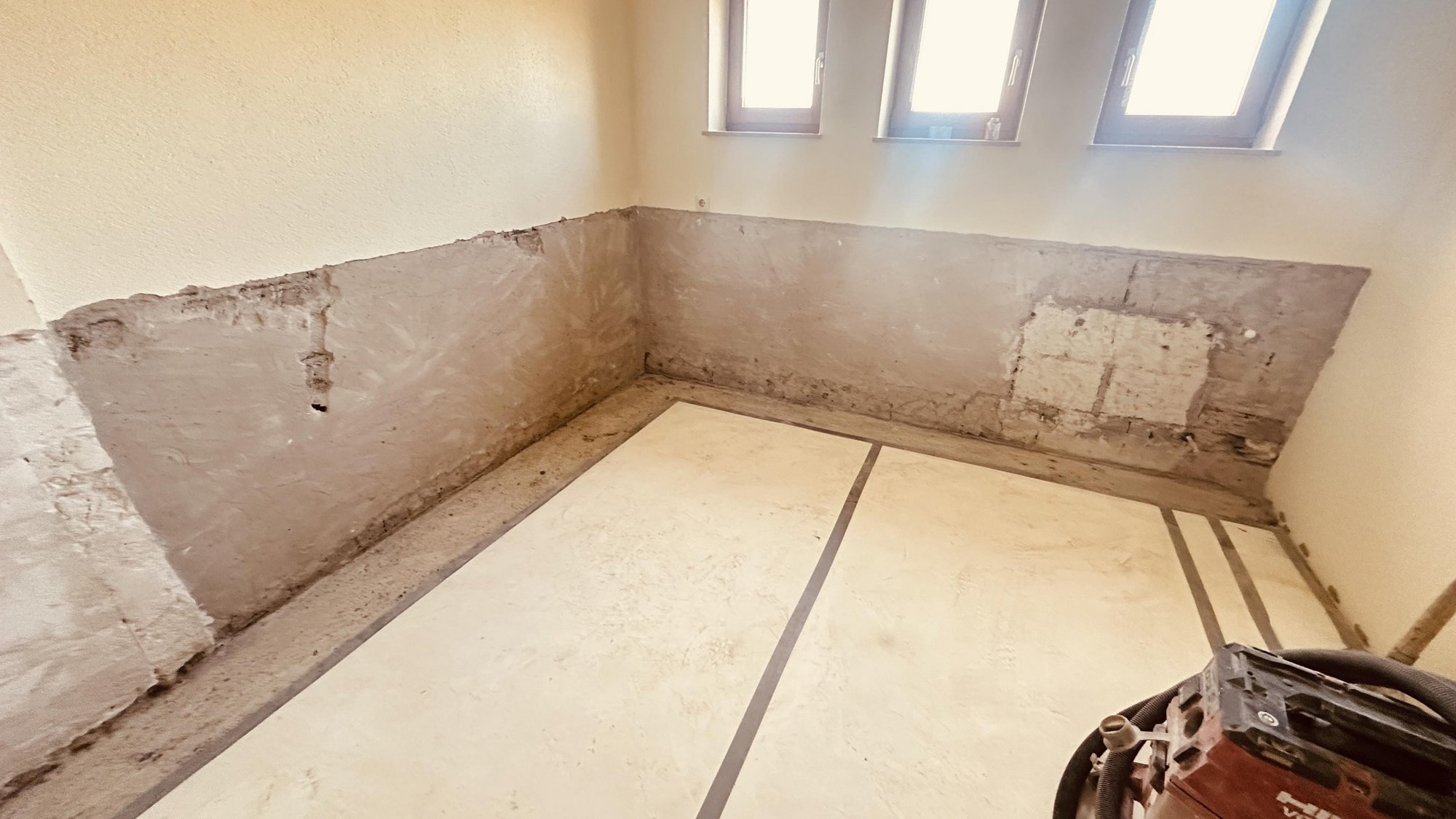 Freigelegte Kellerwand mit abgetragenem Putz, Boden mit Abdeckplatten und Klebeband