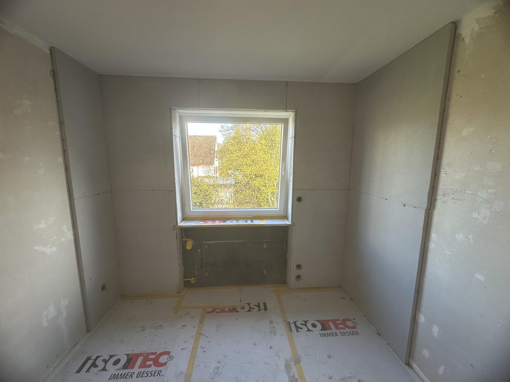 Kleiner Raum mit hellen Platten an Wänden und Boden, Fenster mittig.