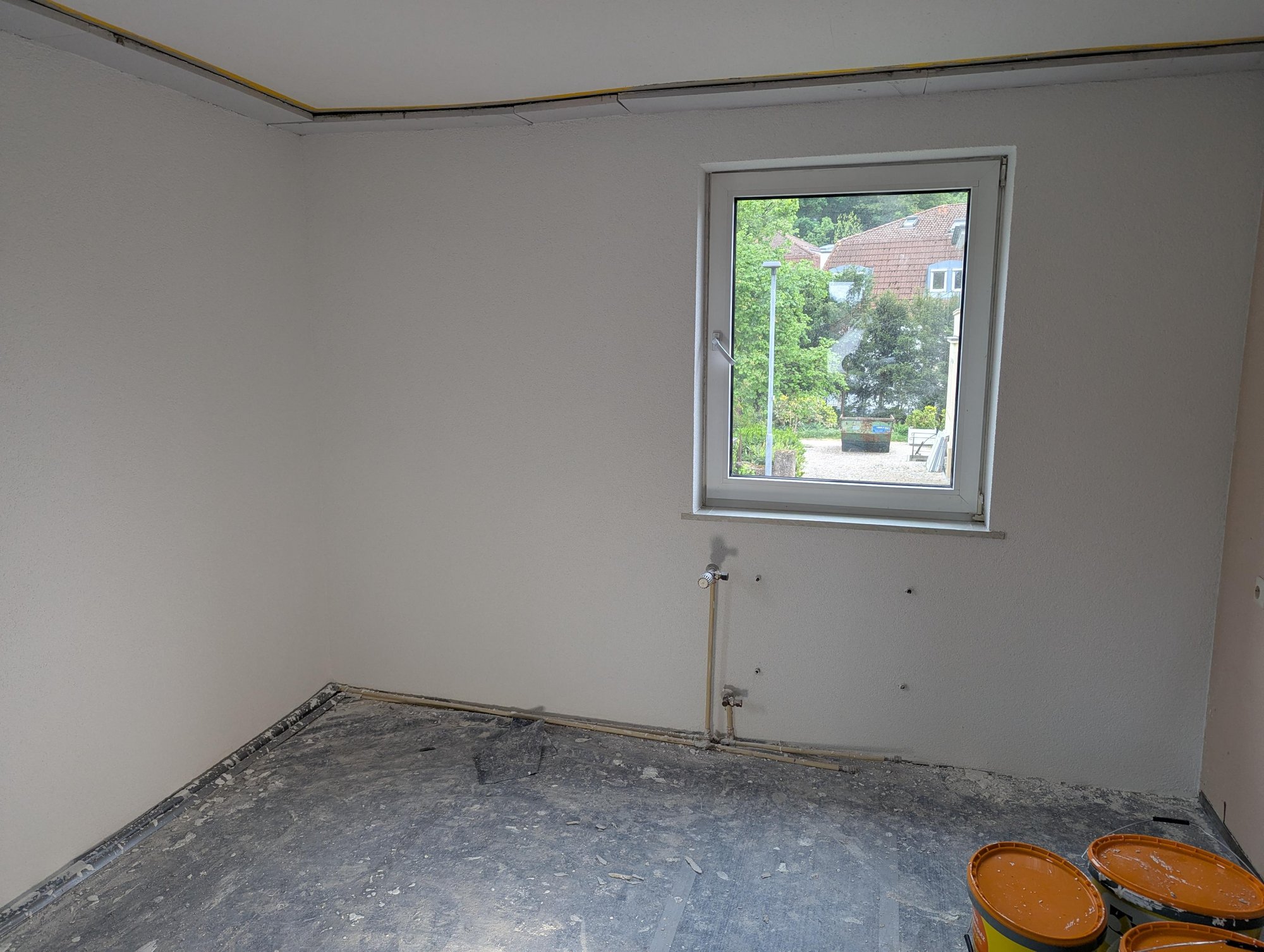 Leerer Raum mit Fenster, freigelegten Rohranschlüssen und abgedecktem Boden.