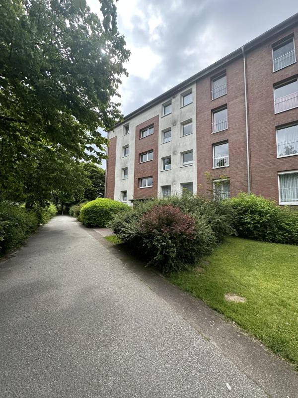 Mehrfamilienhaus mit roter Klinkerfassade am Gehweg, Büsche und Bäume im Vordergrund