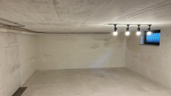 Leerer Kellerraum mit Betonboden, weißen Wänden und kleinem Fenster