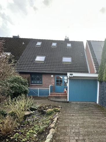 Einfamilienhaus mit dunklem Ziegeldach, blauem Garagentor und Vorgartenweg.