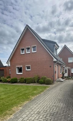 Backsteinhaus mit Giebeldach, gepflasterter Einfahrt und Rasenfläche unter bewölktem Himmel