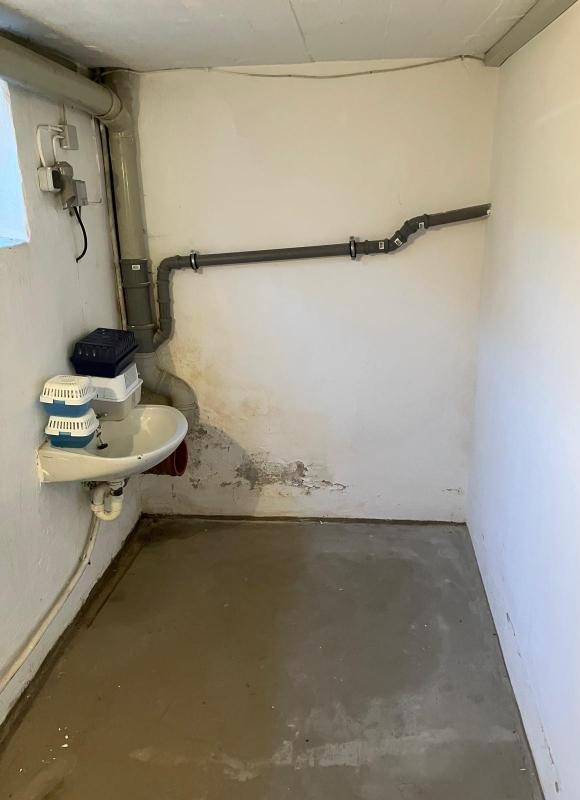 Kleiner Kellerraum mit Waschbecken, Rohrleitungen und Flecken an der Wand