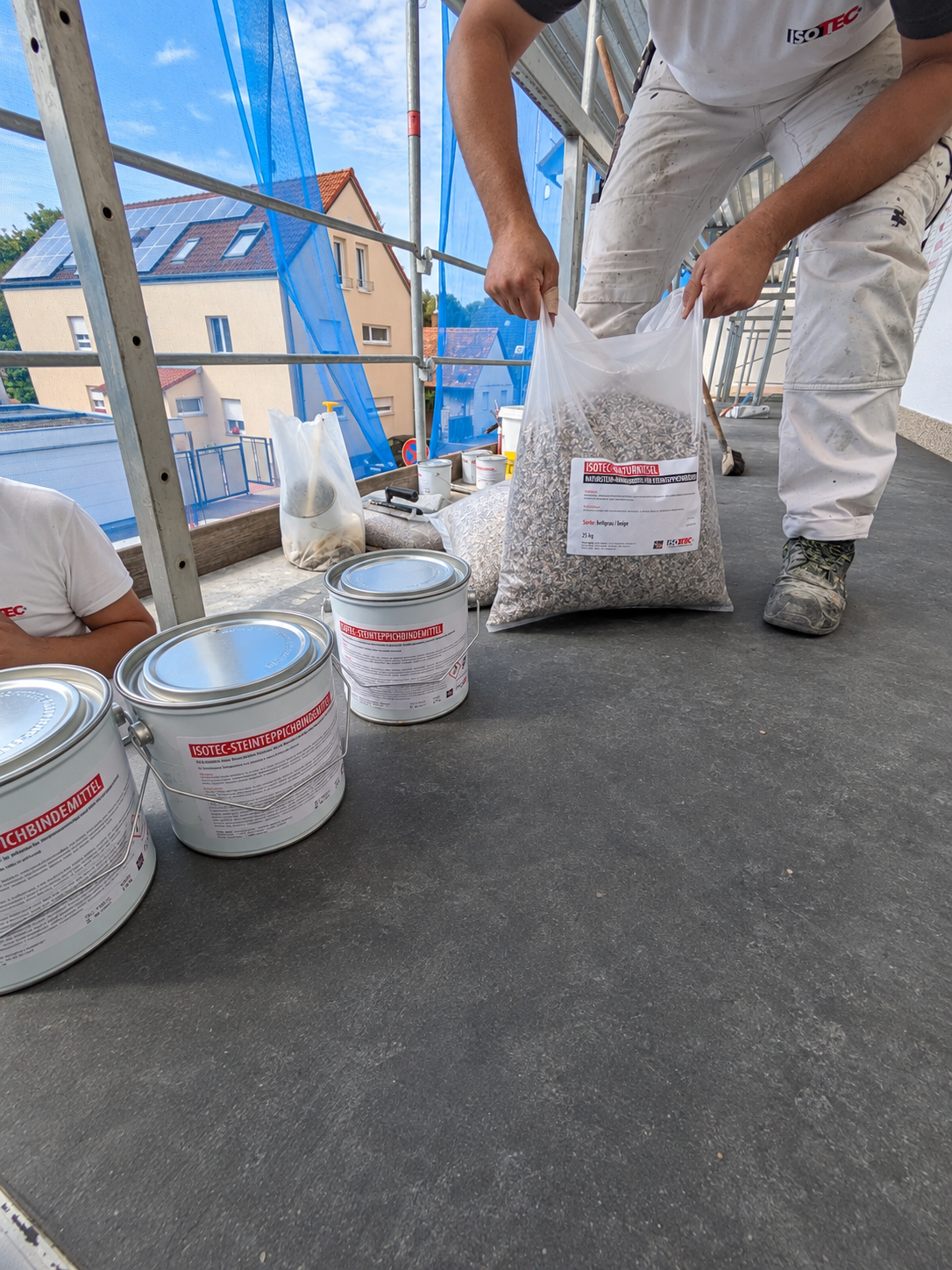ISOTEC Mitarbeiter hält Sack mit grauem Granulat auf Gerüstboden