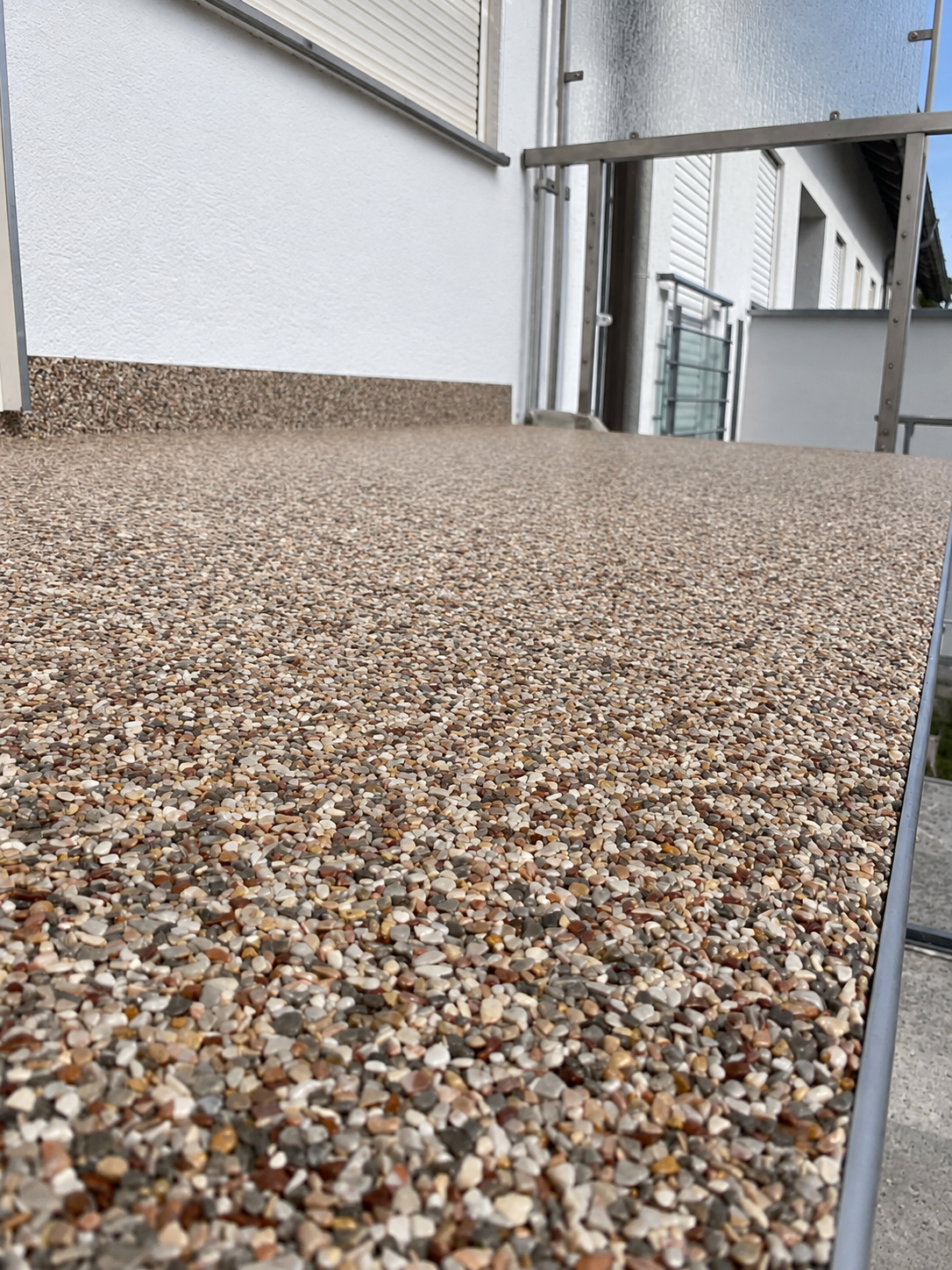 Kiesbelag auf Balkonboden mit Metallgeländer, Blick entlang der Hausfassade