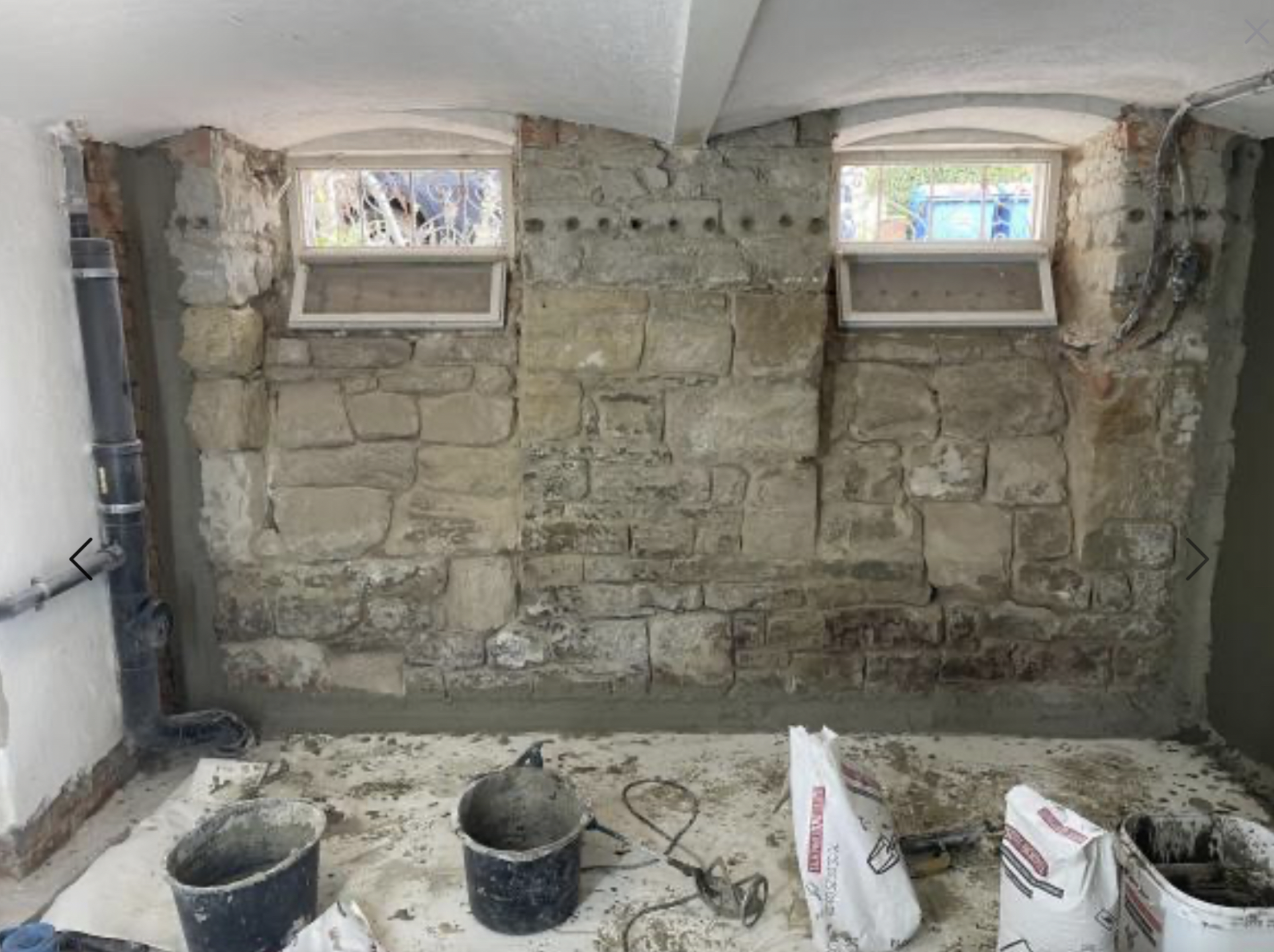 Freigelegte Kellerwand aus Naturstein mit Bohrlöchern und grauer Masse am Boden