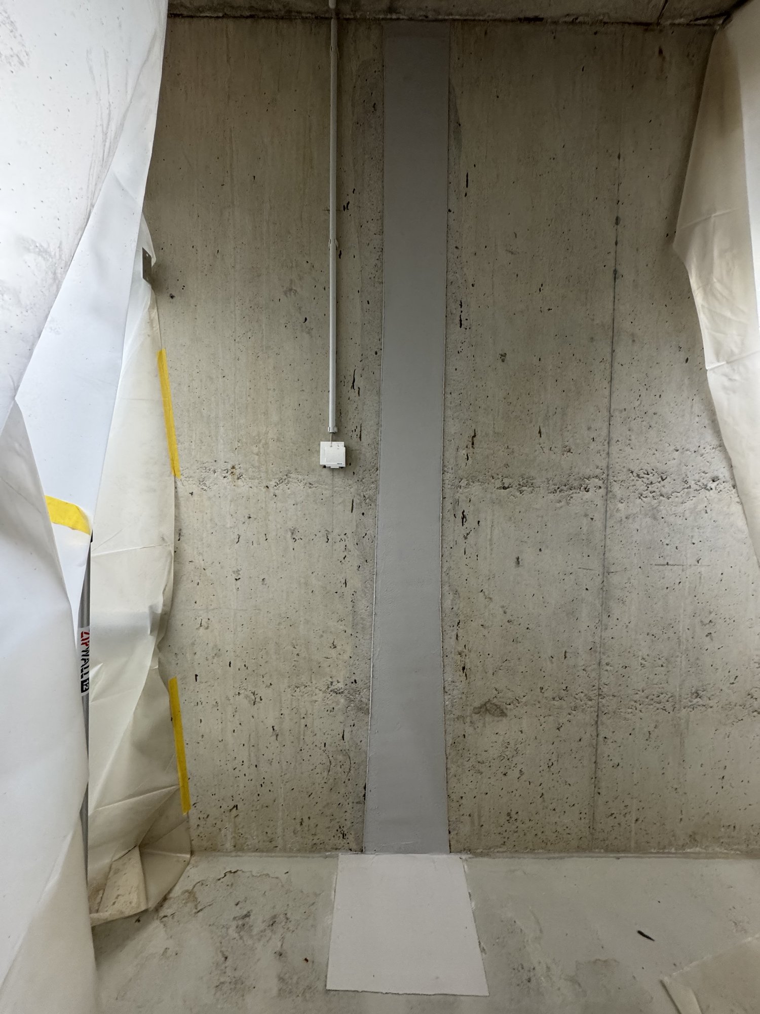 Freigelegte Betonwand mit grauem vertikalen Streifen und abgeklebter Schutzfolie