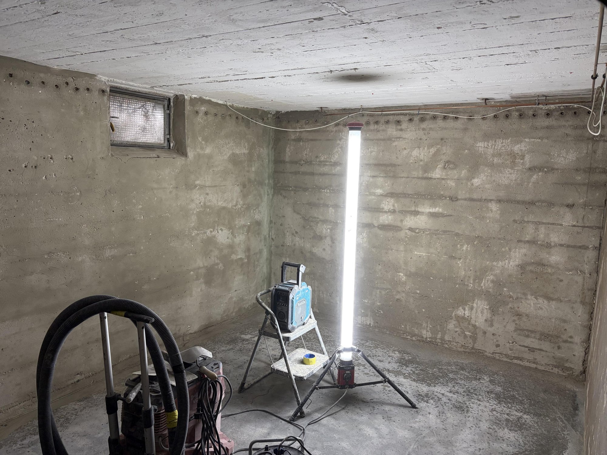 Kellerraum mit Betonwänden, Bohrlochreihe und Baustellenlampe auf Stativ
