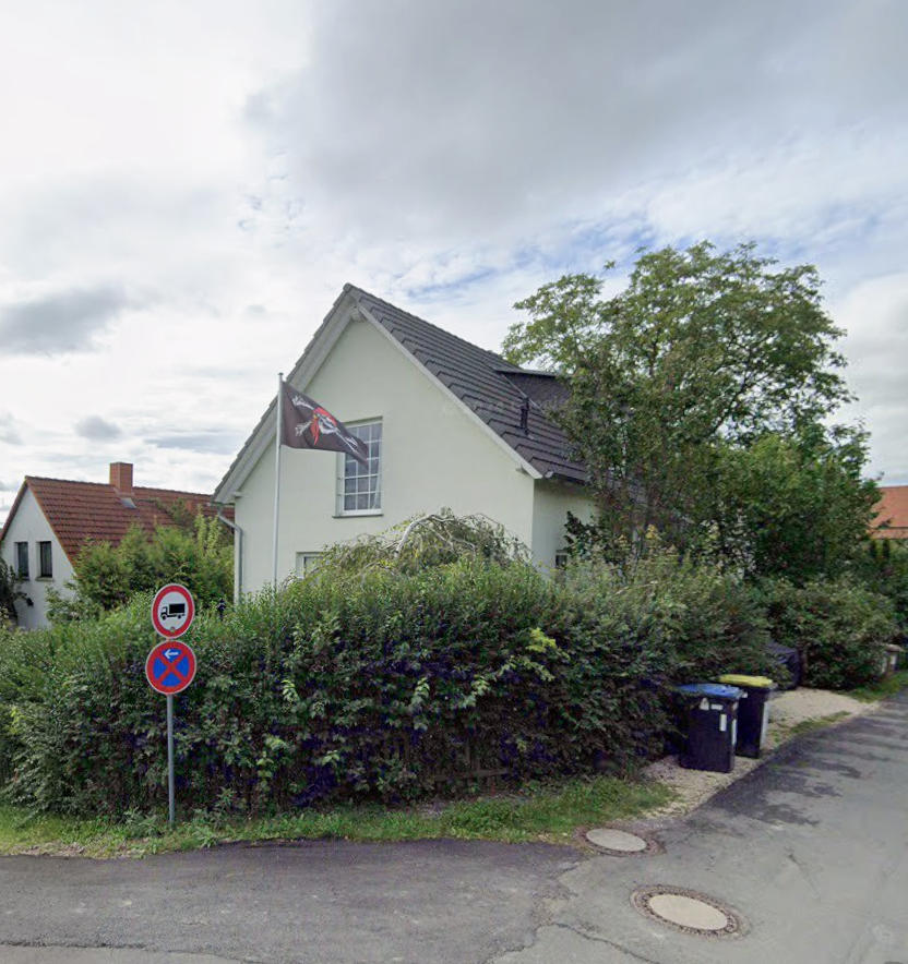 Wohnhaus mit Hecke, Baum und Fahne an einer Straßenecke