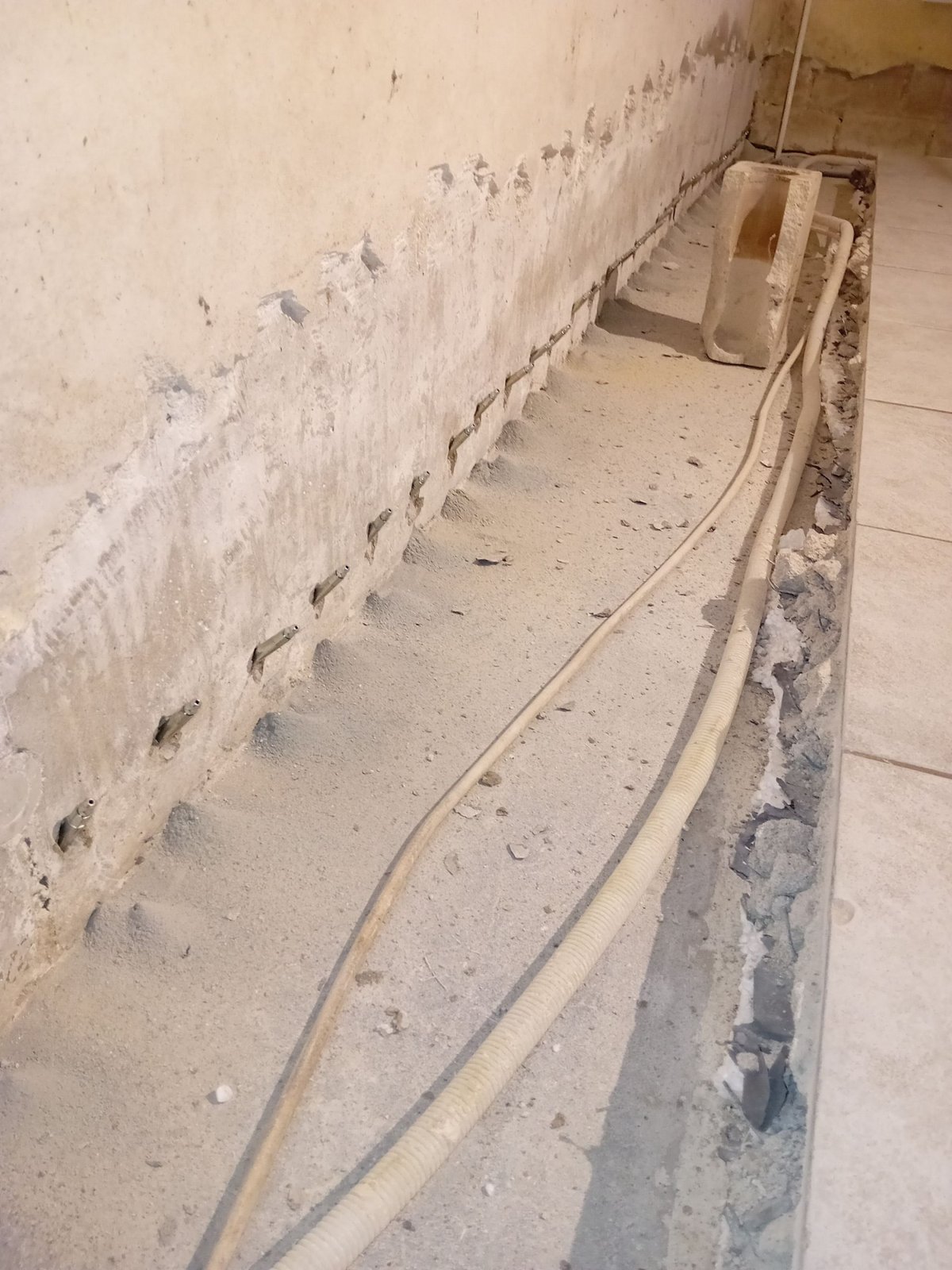 Bohrlochreihe mit Metallpackern an Wand, Kabel und Schutt im Bodenkanal
