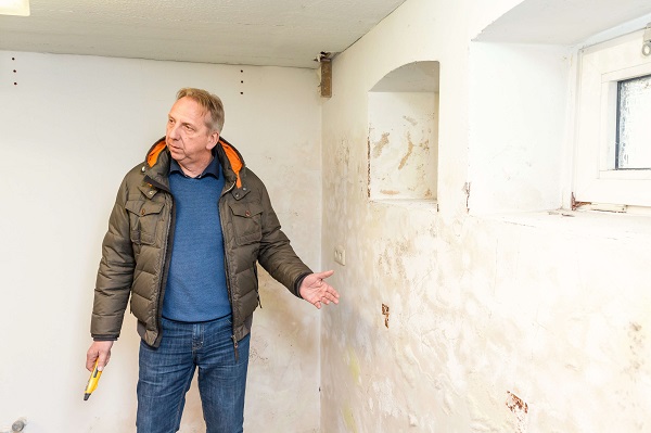 Person zeigt auf beschädigte, fleckige Kellerwand